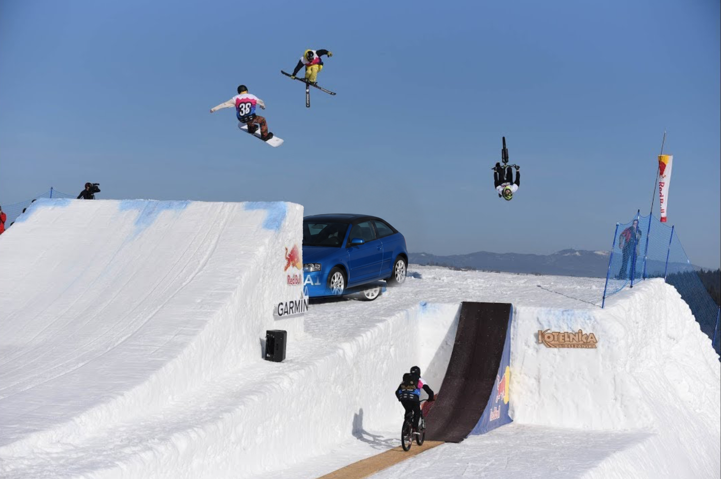 Snowboardzista, narciarz i rowerzysta jednocześnie w powietrzu nad systemem skoczni